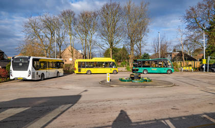 Three buses in a carpark nearby a roundabout. 