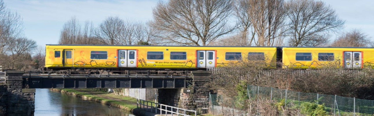 A 507 train travelling over a bridge. There is a river below the bridge. 
