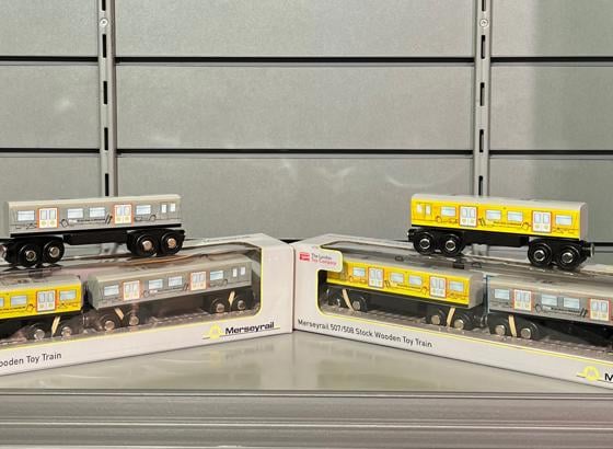 Wooden model toy trains on a shelf. Two trains are placed on top of two cardboard boxes. 