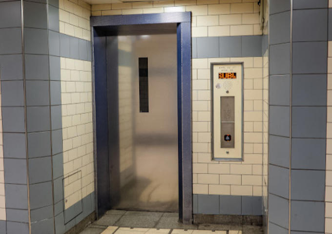 A door of a lift at an underground station. The door is surrounded by tiled walls. 