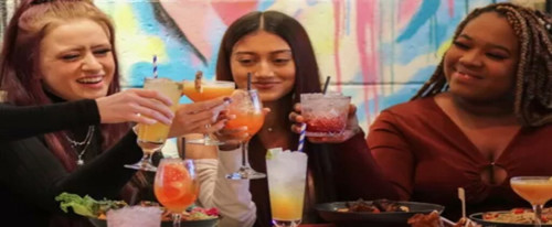 Three girls cheersing brightly coloured cocktails.