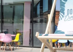 A large deck chair and table and chairs outside, on a sunny day. 