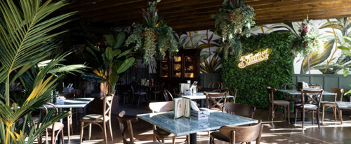 Indoors at The Botanist restaurant. There are tables and chairs and large green plants.