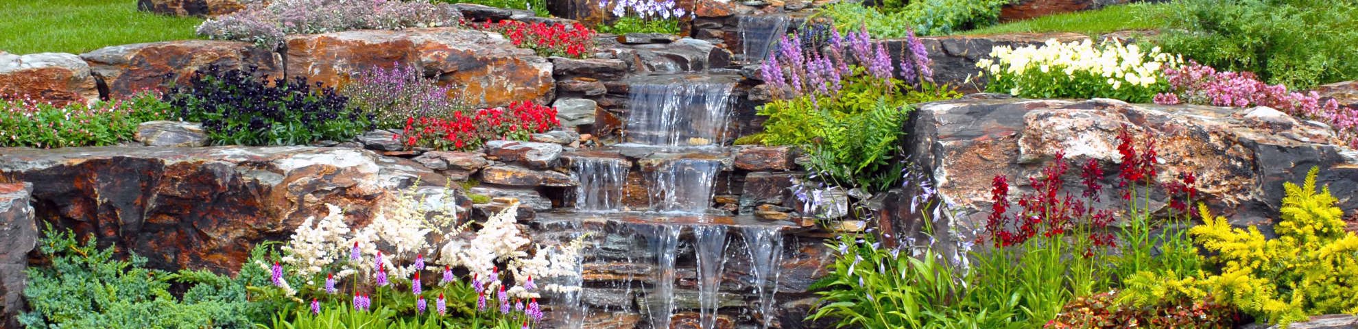 A waterfall outside with brightly coloured flowers.