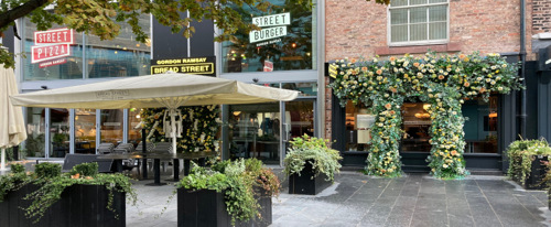 Exterior of restaurant on a sunny day. There are plants and a flower arch.